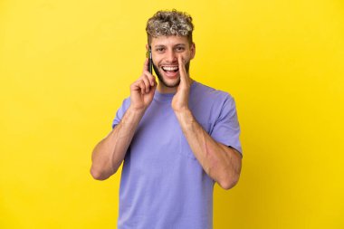 Sarı arka planda izole edilmiş cep telefonu kullanan beyaz bir adam ağzı açık bağırıyor.