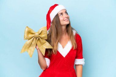 Anne Noel gibi giyinmiş, mavi arka planda izole edilmiş Noel yayını tutan beyaz bir kadın gülümserken yukarı bakıyor.