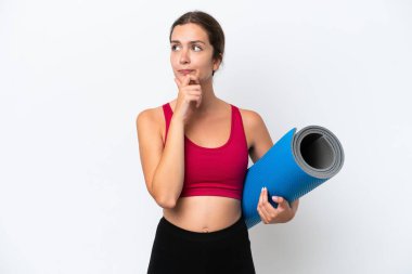 Beyaz arka planda izole edilmiş bir minderi tutarken yoga derslerine giden beyaz bir kadın şüpheleri ve düşünceleri var.