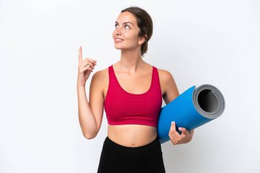 Beyaz arka planda izole edilmiş bir minderi tutarak yoga derslerine giden beyaz bir kadın harika bir fikre işaret ediyor.