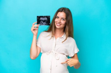Young caucasian woman isolated on blue background pregnant and holding an ultrasound