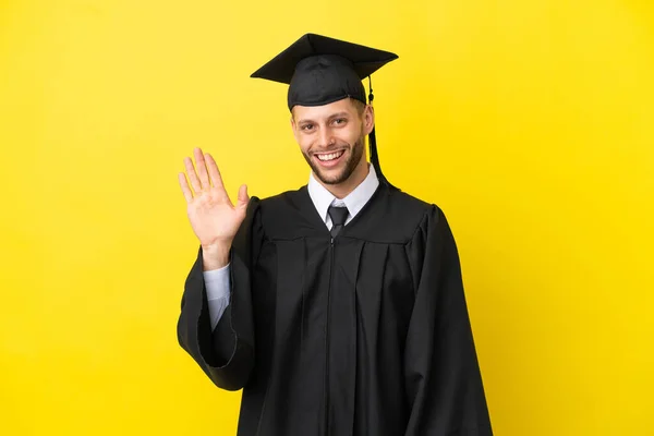 Νεαρός Απόφοιτος Πανεπιστημίου Καυκάσιος Άνδρας Απομονωμένος Κίτρινο Φόντο Χαιρετώντας Χέρι — Φωτογραφία Αρχείου