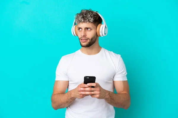 Jeune Homme Caucasien Beau Isolé Sur Fond Bleu Écoutant Musique — Photo