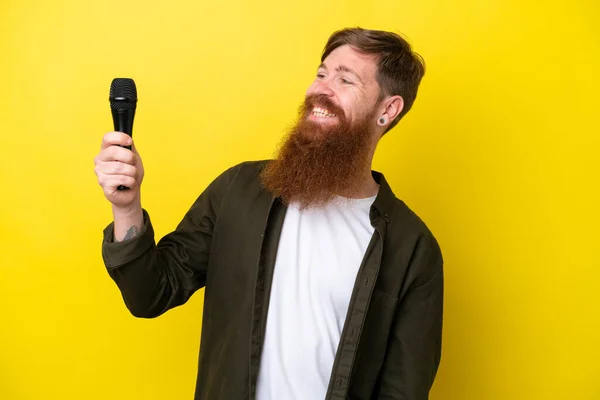 Zrzavý Muž Plnovousem Zvedající Mikrofon Izolovaný Žlutém Pozadí Šťastným Výrazem — Stock fotografie
