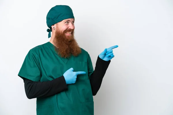 Χειρουργός Κοκκινομάλλης Πράσινη Στολή Απομονωμένος Λευκό Φόντο Δείχνοντας Δάχτυλο Στο — Φωτογραφία Αρχείου