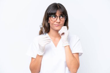 Beyaz arka planda izole edilmiş aletleri tutan beyaz dişçi kadının şüpheleri ve düşünceleri var.