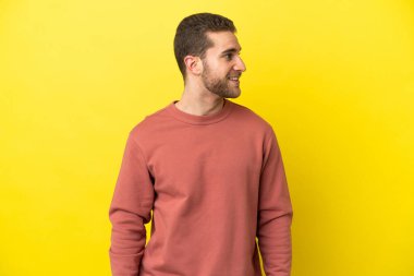 Sarışın yakışıklı adam izole edilmiş sarı arka planda yan tarafa bakıyor ve gülümsüyor.