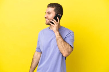 Sarışın yakışıklı adam izole edilmiş sarı arka planda cep telefonuyla sohbet ediyor.