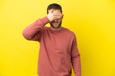 Sarışın yakışıklı adam, izole edilmiş sarı arka planda, gözleri elle kapatıyor. Bir şey görmek istemiyorum.