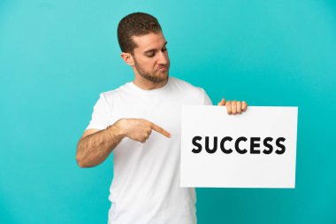 Yakışıklı, mavi arka planda, üzerinde SUCCESS yazan bir pankart tutan ve onu işaret eden bir sarışın.