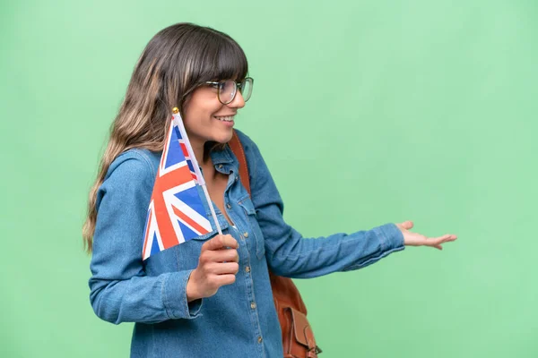 Young caucasian woman holding an United Kingdom flag over isolated background with surprise expression while looking side