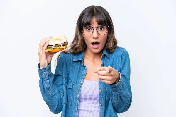 Young Caucasian Woman Holding Burger Isolated White Background Surprised Pointing — Stock Photo, Image