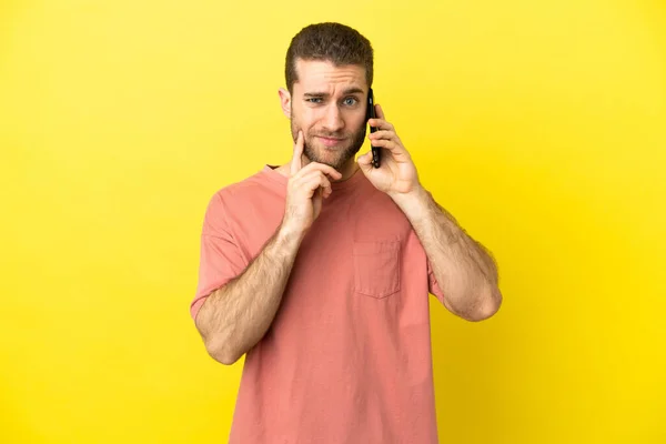 Przystojny Blondyn Korzystający Telefonu Komórkowego Odosobnionym Tle Mając Wątpliwości Podczas — Zdjęcie stockowe
