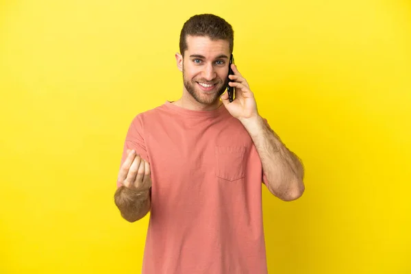 Przystojny Blondynka Człowiek Pomocą Telefonu Komórkowego Odosobnionym Tle Gestem Pieniądze — Zdjęcie stockowe