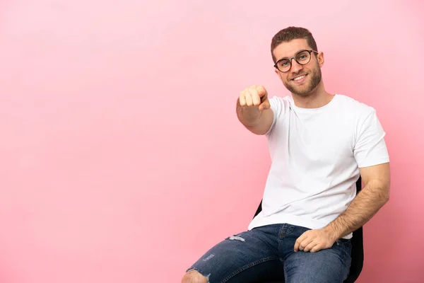 Mladý Muž Sedí Židli Nad Izolované Růžové Pozadí Ukazuje Dopředu — Stock fotografie