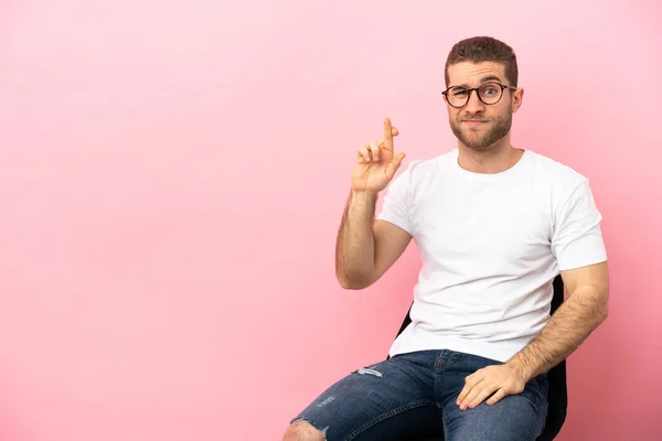 Young Man Sitting Chair Isolated Pink Background Fingers Crossing Wishing — Φωτογραφία Αρχείου