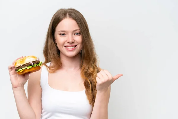 Młoda Ładna Kobieta Trzyma Hamburgera Izolowane Białym Tle Wskazując Stronie — Zdjęcie stockowe