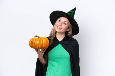 Cadı gibi giyinmiş, elinde balkabağı olan genç sarışın bir kadın beyaz arka planda izole edilmiş bir şekilde yukarı bakarken bir fikir düşünüyor.