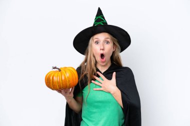 Cadı gibi giyinmiş, beyaz arka planda balkabağı tutan genç sarışın kadın şaşırdı ve şaşırdı.