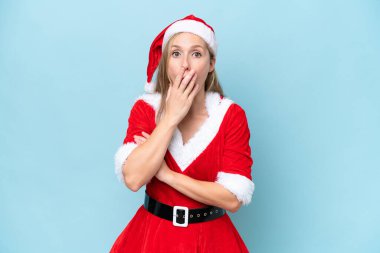 Anne Noel Baba gibi giyinmiş genç sarışın kadın mavi arka planda izole edilmiş, sağa bakarken şaşırmış ve şok olmuştu.