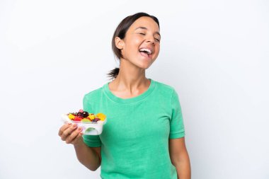 Beyaz arka planda bir kase meyve tutan genç İspanyol kadın gülüyor.