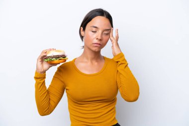 Beyaz arka planda başı ağrıyan bir burger tutan genç İspanyol kadın.