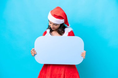 Anne Noel gibi giyinmiş genç İspanyol kadın mavi arka planda izole edilmiş, elinde boş bir konuşma balonu var.