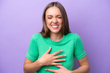 Mor arka planda izole edilmiş genç beyaz kadın çok gülümsüyor.