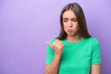 Mor arka planda izole edilmiş genç beyaz kadın mutsuzdu ve yan tarafı gösteriyordu.