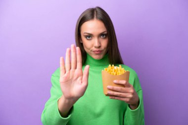 Mor arka planda kızarmış cips tutan beyaz bir kadın dur hareketi yapıyor.
