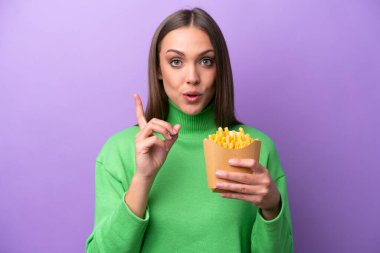 Mor arka planda kızarmış cips tutan beyaz bir kadın çözümü bulmak için parmağını kaldırıyor.