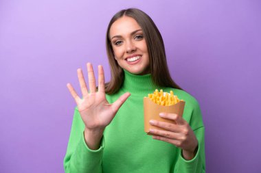 Mor arka planda kızarmış cips tutan genç beyaz kadın parmaklarıyla beşi sayıyor.