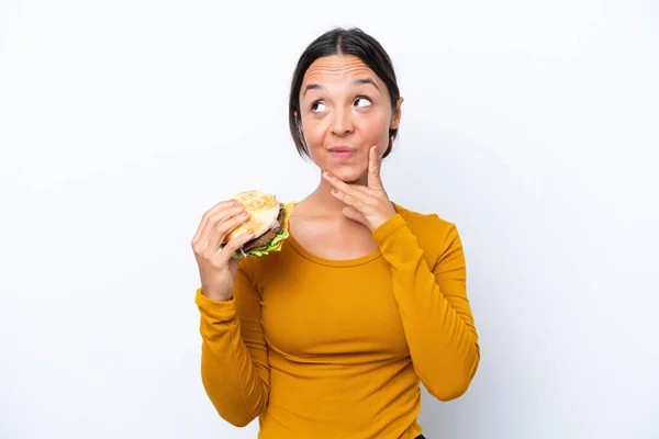 Młoda Latynoska Kobieta Trzyma Hamburgera Białym Tle Myśląc Pomysł Patrząc — Zdjęcie stockowe