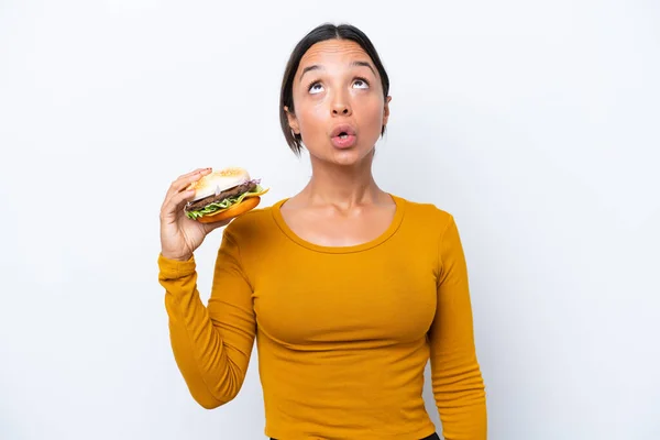 Young Hispanic Woman Holding Burger Isolated White Background Looking Surprised — Stock Photo, Image