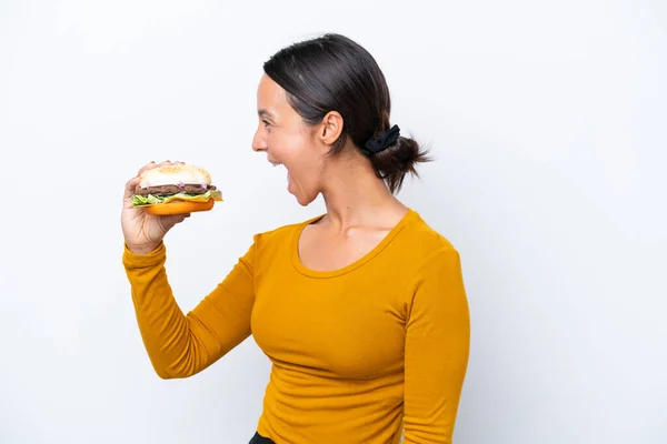 Młoda Latynoska Trzyma Hamburgera Białym Tle Śmiejąc Się Pozycji Bocznej — Zdjęcie stockowe