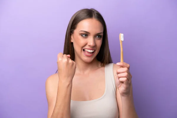 Young caucasian woman brushing teeth isolated on purple background celebrating a victory