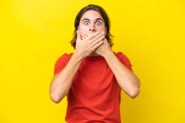 Beyaz tenli yakışıklı adam sarı arka planda izole edilmiş ağzı elleriyle kapatıyor.