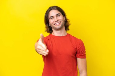 Beyaz tenli yakışıklı adam sarı arka planda izole edilmiş ve iyi bir anlaşma için el sıkışıyor.