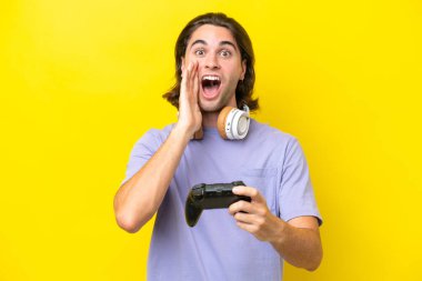 Sarı arka planda, şaşırmış ve şok olmuş bir yüz ifadesiyle video oyunu kontrolörüyle oynayan yakışıklı beyaz bir adam.