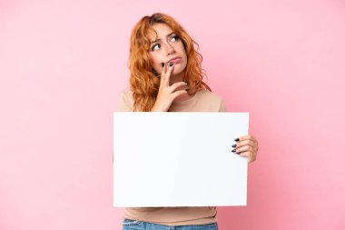 Kafkasyalı genç bir kadın pembe arka planda izole edilmiş elinde boş bir levhayla düşünüyor.