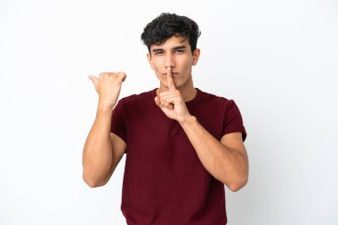 Beyaz arka planda izole edilmiş genç Arjantinli bir adam, kenarı işaret ediyor ve sessizlik hareketi yapıyor.