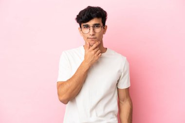 Arjantinli genç bir adam pembe arka planda soyutlanmış düşünüyor.