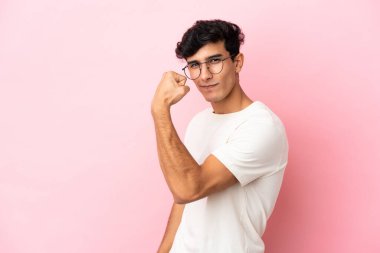 Pembe arka planda izole edilmiş genç Arjantinli adam güçlü bir jest yapıyor.
