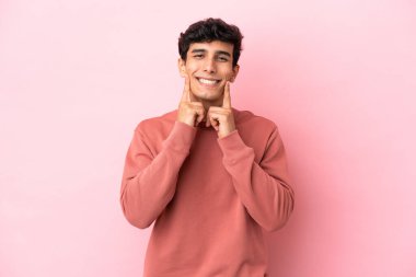Arjantinli genç adam pembe arka planda izole edilmiş mutlu ve hoş bir ifadeyle gülümsüyor.