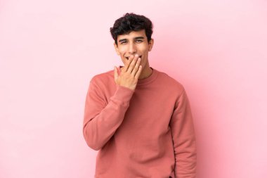 Arjantinli genç bir adam pembe arka planda izole edilmiş mutlu ve gülümseyen bir ağızla elini kapatıyor.