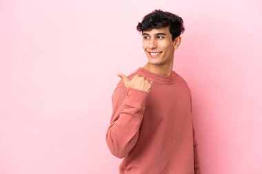 Pembe arka planda izole edilmiş genç Arjantinli bir adam bir ürün sunmak için kenarı işaret ediyor