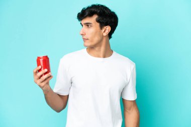 Arjantinli genç adam mavi arka planda izole edilmiş bir içecek tutuyor.