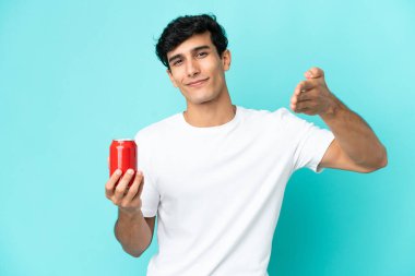 Arjantinli genç adam mavi arka planda izole edilmiş bir içecek tutuyor ve iyi bir anlaşma için el sıkışıyor.