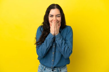 Sarı arka planda izole edilmiş genç beyaz kadın mutlu ve gülümseyen elleriyle ağzını kapatıyor.