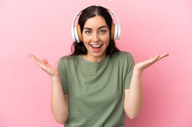 Pembe arka planda izole genç beyaz kadın şaşırdı ve müzik dinliyor.